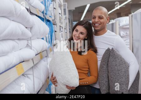 Schönes multirassisches Paar, das neue Kissen im Geschäft für Haushaltswaren kauft. Charmante Frau einkaufen für Bettwäsche mit ihrem schönen Freund Stockfoto