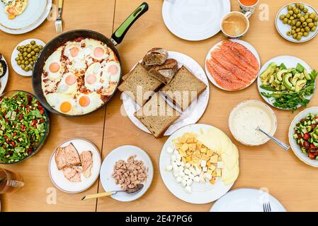Gesundes Frühstück mit der Familie. Draufsicht. Servieren von Eiern, Brot, Avocado, geräuchertem Lachs, Käse und Salat aus frischem Gemüse auf einem Holztisch, Stockfoto