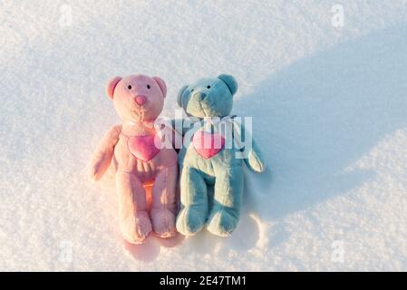 Zwei kleine Teddybären liegen flach auf einem Schnee am sonnigen Winterabend.Valentinstag Konzept. Stockfoto