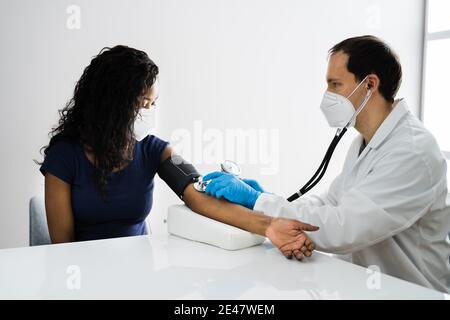 Afrikanischer Patient Blutdruck-Check-Up Trägt Gesichtsmaske Stockfoto