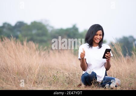 Schöne helle Haut afrikanische Frau lächelt, während sie Telefon und gibt Daumen nach oben in Richtung der Kamera Stockfoto