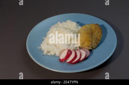 Gekochter weißer Reis mit Fischschnitzel in Speck auf einem grauen Hintergrund blauen Teller eingewickelt. Fischball mit Reisgarnieren und Rettich. Stockfoto