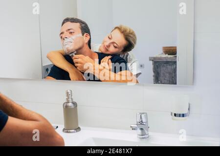 Junges Paar zu Hause im Schlafzimmer, während Mann tun Und schneiden Sie Bart bereit, den Tag zu beginnen - Liebe Leute Indoor Freizeitbeschäftigung - Freundin umarmen Freund Stockfoto