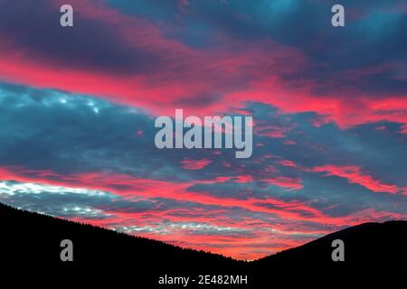 Szenische dramatische feurig bewölkt Sonnenuntergang Abend Blick über Bergresort Dorf Bukovel in der Ukraine mit Kiefernwald weihnachtsbaum Silhouetten. Wunderschön Stockfoto