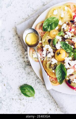 Frischer, heller Tomatensalat aus bunten Tomaten mit Feta-Käse, Basilikum und Olivenöl. Vegetarische und vegane Speisen. Konzept für ein schmackhaftes und gesundes Mea Stockfoto