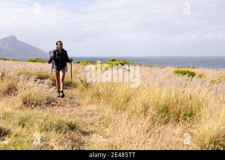 Fit afroamerikanische Frau trägt Rucksack nordic Walking an der Küste Stockfoto