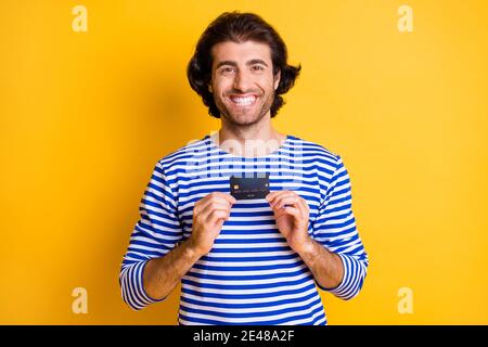 Foto von positiven mittleren östlichen Kerl halten Kreditkarte tragen Blau weiße nautische Weste isoliert auf glänzendes gelbes Farbhintergrund Stockfoto