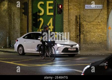 Neben dem Rush Hour-Verkehr fährt eine Radfahrerin unter der Eisenbahnbrücke an der Ecke Herne Hill und Milkwood Road in SE24 und am 21. Januar 2021 in London, England. Herne Hill liegt zwischen Brixton, Dulwich Village und Camberwell und liegt über den gemeinschaftlich genutzten Londoner Stadtbezirken Lambeth und Southwark mit einer Gemeinde von ca. 15,000. Stockfoto