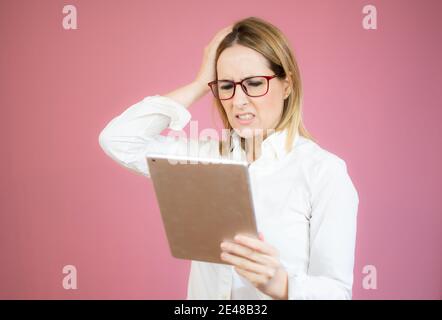 Junge hübsche Frau, die mit zweifelhaftem und skeptischem Ausdruck auf eine Tablette schaut. Stockfoto