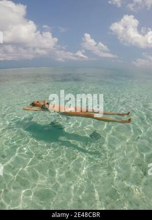 Junge schöne Frau liegt und schwimmt auf dem Rücken in türkisfarbenem Meerwasser am tropischen Paradiesstrand in Bora Bora Insel, Französisch Polynesien.Urlaub und Stockfoto