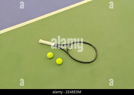 Draufsicht auf Tennisschläger und zwei Bälle auf dem grünen Sandtennisplatz. Stockfoto