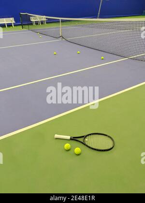 Nahaufnahme des Tennisschlägers und zweier Bälle auf dem grünen Sandtennisplatz. Stockfoto