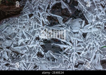 Abstrakter Winterhintergrund, rissige Eis auf gefrorener Pfütze. Eisfragmente auf gefrorenem Wasser. Das Eis zerbrochene Stücke.Eis auf einer gefrorenen Wasserpfütze im Winter Stockfoto