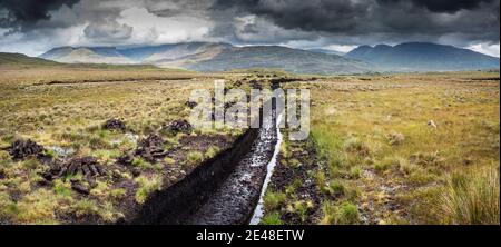 Torfstapel (Rasen) zum Heizen, Trocknen auf gesägter Moor in Bunowen, in der Nähe von Killar Harbor, Connemara, Grafschaft Galway, mit Mweelrea Mountains in der Ferne Stockfoto