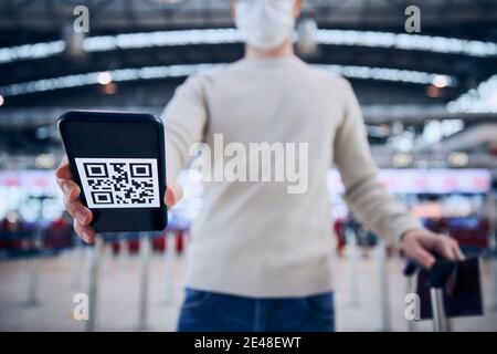 Fahren Sie im neuen Normalzustand. Mann mit Gesichtsmaske und Smartphone mit QR-Code am Flughafen. Themen Verifikation der Immunisierung nach der Impfung wit Stockfoto