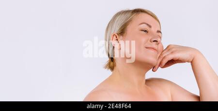 Banner. Ältere Frau mit feuchtigkeitsspendender Haut nach kosmetischen Verfahren lächelt und schaut zur Seite, sanft berühren die Haut ihres Gesichts. Weiß Stockfoto