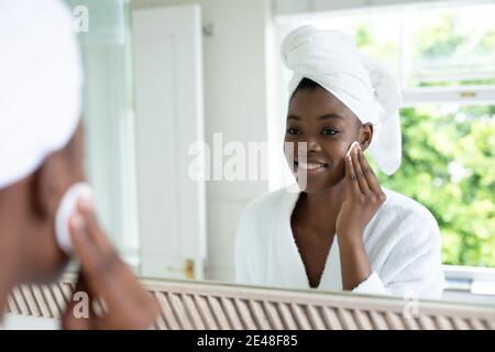 afroamerikanische Frau im Bademantel Entfernen Make-up beim Blick in Der Spiegel im Badezimmer Stockfoto