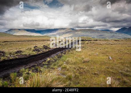 Torfstapel (Rasen) zum Heizen, Trocknen auf gesägter Moor in Bunowen, in der Nähe von Killar Harbor, Connemara, Grafschaft Galway, mit Mweelrea Mountains in der Ferne Stockfoto