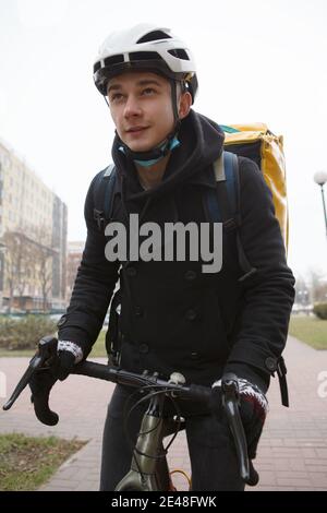 Vertikale Aufnahme eines jungen Mannes, der im Lieferservice arbeitet, Fahrrad in der Stadt reitet, im Thermorucksack trägt Stockfoto