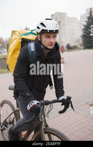 Vertikale Aufnahme eines jungen Lieferers mit Thermorucksack Fahrrad fahren Stockfoto