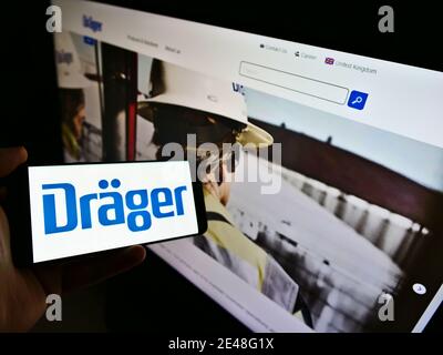 Person, die Smartphone mit Logo des deutschen Ingenieurunternehmens Dräger AG auf dem Bildschirm vor der Website hält. Fokus auf der linken Seite des Handydisplays. Stockfoto