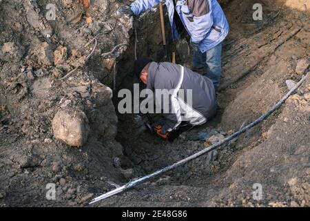 Mann schneidet dicken elektrischen Draht in einem Graben in den Boden. Stockfoto