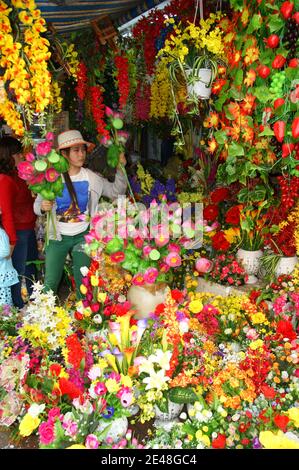 Vietnamesische Floristin montiert einen bunten Bund aus Kunststoff, Seide und Pappmaché Blumen. Stockfoto