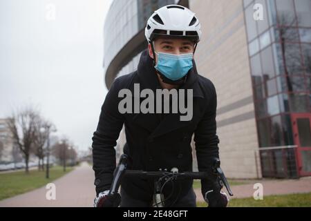 Low-Winkel-Aufnahme eines Mannes mit medizinischer Gesichtsmaske Und schützenden Fahrradhelm während des Fahrradfahrens Stockfoto