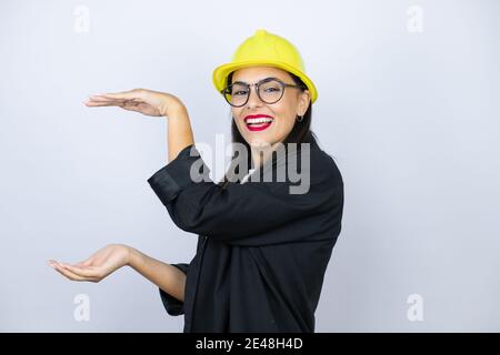 Junge Architektin Frau trägt Hardhat gesturing mit Händen zeigt große und große Größe Zeichen, Maßnahme Symbol. Lächelnd. Messkonzept. Stockfoto