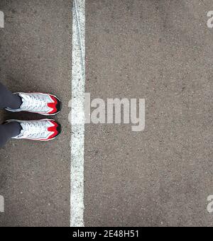 Füße in Turnschuhen stehen nahe der Trennlinie auf dem Asphalt. Begrenzungslinie, soziale Distanz, Warten in der Schlange. Die Grenze, stehen in der Schlange für einen Anfang. Stockfoto