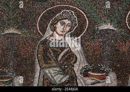 Unter einem Juwelier-Diadem blickt eine von 22 prächtig gekleideten weiblichen christlichen Heiligen in einer Prozession. Detail aus dem byzantinischen Mosaik, das in den 500er Jahren n. Chr. in der Basilica di Sant’Apollinare Nuovo in Ravenna, Emilia-Romagna, Italien, geschaffen wurde. Stockfoto