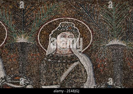 Feierliches Gesicht einer von 22 prächtig gekleideten weiblichen christlichen Heiligen, die in einer Prozession spazieren gehen. Detail aus dem byzantinischen Mosaik, das in den 500er Jahren n. Chr. in der Basilica di Sant’Apollinare Nuovo in Ravenna, Emilia-Romagna, Italien, geschaffen wurde. Stockfoto