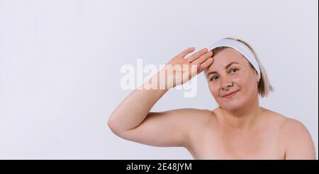 Banner. Eine ältere Frau in einem weißen Verband und mit Feuchtigkeit versorgt Haut nach Hause Verfahren schaut in eine Kamera auf einem grauen Hintergrund. Stockfoto