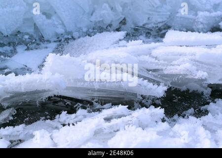 Eisstücke bedeckt mit weißem Schnee auf einem wieder gefrorenen Gewässer. Winter in Osteuropa. Hintergrundstruktur. Horizontale Ausrichtung. Stockfoto