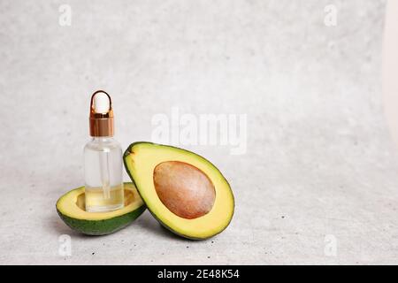 Avocado-Öl in einer Glasflasche und frische Avocado auf Grauer Hintergrund mit Kopierbereich Stockfoto