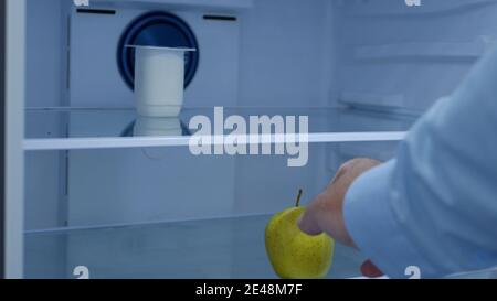 Hungriger Mann öffnet den leeren Kühlschrank auf der Suche nach Nahrung und Nehmen Sie einen Apfel Stockfoto