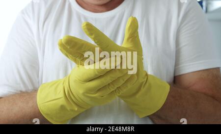 Der Mensch legt seine gelben Schutzhandschuhe auf die Hände, um sich vorzubereiten So beginnen Sie mit der Reinigung in der Küche und im Badezimmer Stockfoto