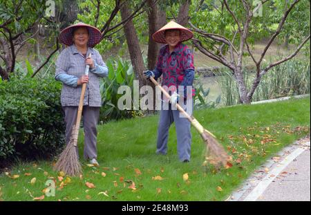 Zwei Damen, die in einem Park Blätter putzen und räumen, teilen ein Lächeln und lachen mit mir, während ich ihr Foto mache. Stockfoto