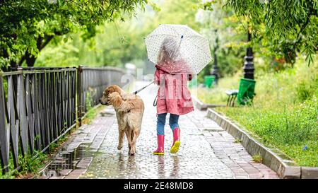 Kleines Mädchen, der Hund unter Regen läuft Stockfoto