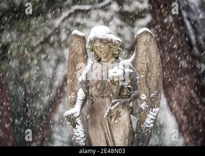 Statue des Engels Grabstein im prognostizierten Winterschnee friedlicher Schneefall Dezember Friedhof mit Flügeln Grabstein und Wald auf der Spitze angesiedelt Flügel Stockfoto