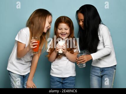 Glückliche Mädchen Freunde Kinder in weißen T-Shirts mit Textraum stehen und halten Wasser, Milch oder Kefir und frischen Karottensaft Stockfoto