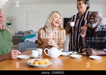 Ältere kaukasische und afroamerikanische Paare sitzen am Tisch und trinken Tee zu Hause Stockfoto