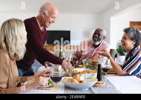 Ältere kaukasische und afroamerikanische Paare sitzen am Tisch beim Essen Abendessen zu Hause Stockfoto