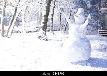 Großer Schneemann im Hof nach einem Schneefall im Winter. Nase-Karotte, Eimer auf dem Kopf, Handschuhe an den Händen, Augen. Autos im Schnee entlang der Straße. Übertrumpfer Stockfoto