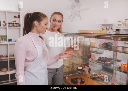 Weibliche Konditorei hilft ihrem Kunden Dessert aus dem Einzelhandel Display wählen, kopieren Raum Stockfoto