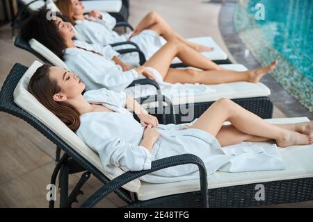 Drei Frauen faulenzen auf Sonnenliegen am Pool Stockfoto