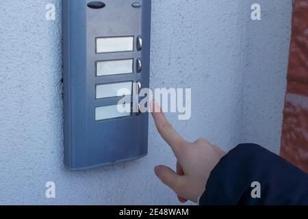 Die Frau klingelt an der Tür. Die weibliche Hand drückt eine Taste an der Türklingel. Stockfoto
