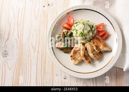 Gebratene Hähnchenscheiben mit Blumenkohlreis, Pilzragout und Tomaten, auf einem leichten Holztisch, gesundes Abnehmen mit Low Carb Diät, Copy Space, Hi Stockfoto