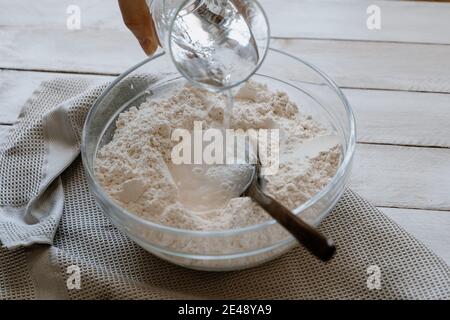 Wasser über Mehl in eine Schüssel gießen, um Brotteig zu machen. Hausgemachtes Brot Stockfoto