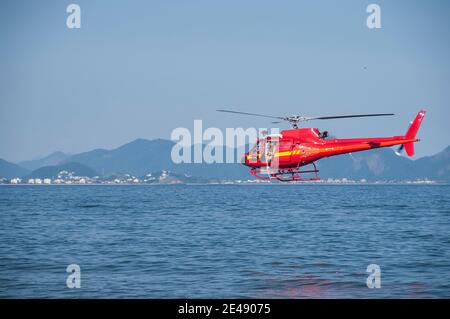 Ein Rettungshubschrauber der Strandwache fliegt über das Meer in der Nähe von Ipanema Beach, Brasilien. Im Hintergrund Zuckerbrot Berg und Copacabana Strand Stockfoto